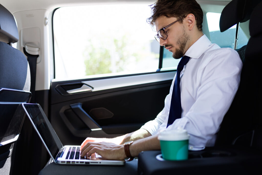 Business man on a laptop working in the back of a car