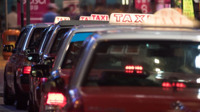 A row of taxi cabs lined up in a busy city at night